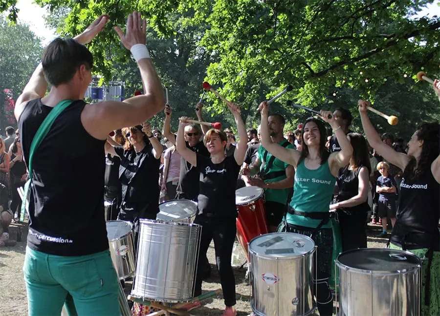 Eine Trommelgruppe mit mehreren Mitgliedern, die in einem Park auftritt und verschiedene Percussion-Instrumente spielt.