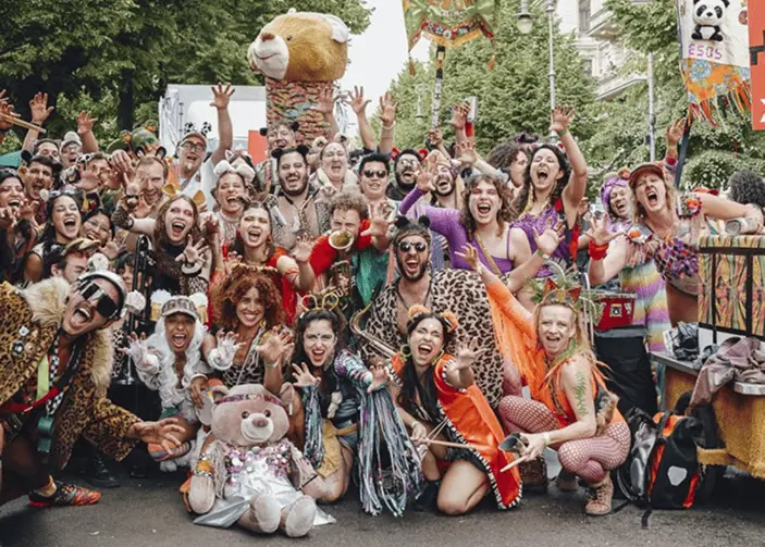 Eine große Gruppe von Menschen in bunten Kostümen, die fröhlich posieren und feiern, umgeben von festlicher Dekoration.